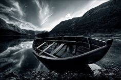 a boat sitting on top of a lake next to a mountain covered in clouds and rocks