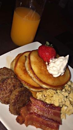 a plate with pancakes, eggs, bacon and strawberries next to a glass of orange juice