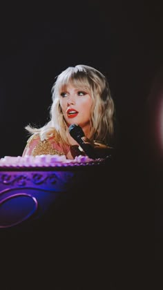 a woman with long blonde hair holding a microphone in front of a purple bowl that has writing on it