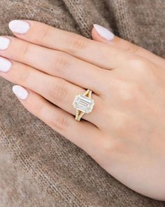 a woman's hand wearing a gold and white ring with a baguette on it