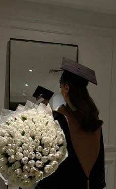 a woman wearing a graduation cap and gown holds a bouquet of white roses in front of a mirror