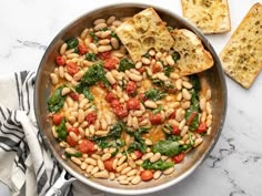 a pan filled with beans and spinach next to slices of bread