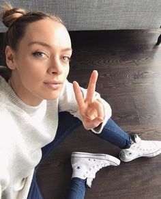 a young woman sitting on the floor making a peace sign with her hand while wearing white sneakers