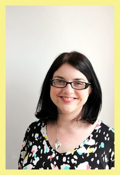 a woman with glasses smiling for the camera in front of a white wall and yellow frame