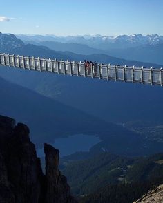 people standing on a glass walkway above the mountains