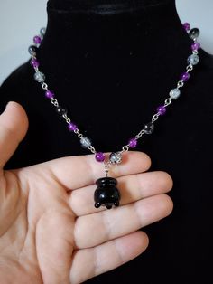 Hand made by Me: a purple beaded necklace that adjusts up to about 20 inches. The necklace features beads in the colors purple and black with a black cauldron charm at the end.  The beads are all made from glass and the necklace has silver colored hardware. Purple Beaded Necklace, Black Cauldron, Purple Bead Necklace, The Black Cauldron, Colors Purple, Hand Beading, Chicago Il, Made By Me, Purple And Black