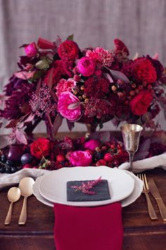 the table is set with red and pink flowers, silver utensils, and napkins