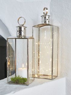 two glass lanterns with candles in them on a shelf