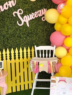 there is a yellow and pink party with balloons on the wall next to a white chair