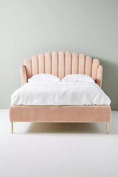 an upholstered bed with white sheets and pink velvet headboard, in front of a gray wall