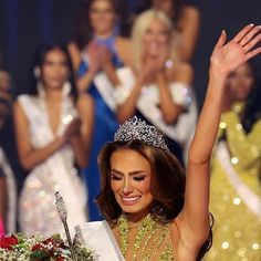 a woman in a tiara waves to the crowd as she holds her hand up