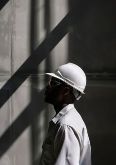 a man wearing a white hard hat standing in front of a wall with shadows on it