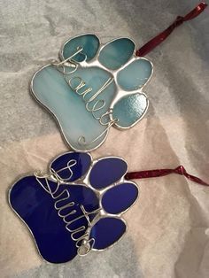 two blue and white dog paw ornament hanging from a red ribbon on top of a bed