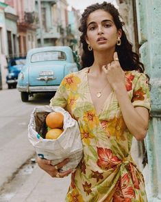 a woman standing on the side of a street holding a bag and fruit in her hand