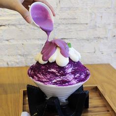 a person pouring purple and white icing on top of a cake in a bowl