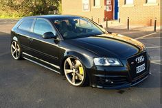 a black car parked in front of a building on the side of the road with yellow rims