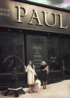 two women and a dog are standing in front of a store with the words paul on it