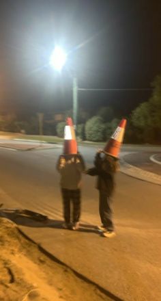 two people standing in the street with traffic cones on their heads and one person holding his hand