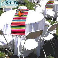 there are many white chairs and tables with colorful tablecloths on them in the grass