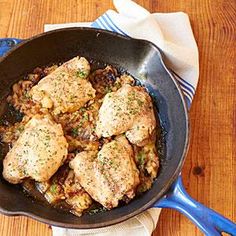 chicken in a skillet on a wooden table with a blue spatula and napkin