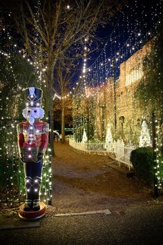 a lighted nutcracker stands in the middle of a park at night with trees and lights all around it