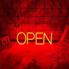 an open neon sign sitting in the middle of a room with books on the floor