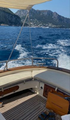 the back deck of a sailboat with mountains in the background and water below it