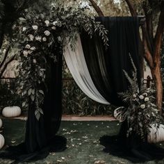 a black and white wedding arch decorated with flowers, greenery and pumpkins on the ground