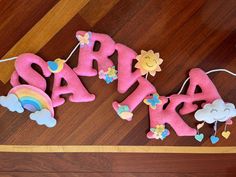 the word baby spelled out in pink felt with rainbows and stars on it, sitting on a wooden floor