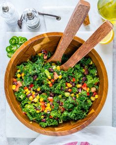 a wooden bowl filled with vegetables next to a glass of wine and two spoons