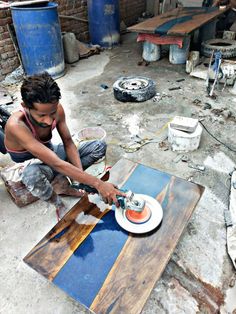 a man sitting on the ground working on a piece of wood with a paintbrush