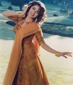 a woman in an orange and gold dress posing for the camera with her hands on her head