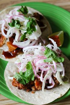 two tacos on a green plate topped with onions and cilantro