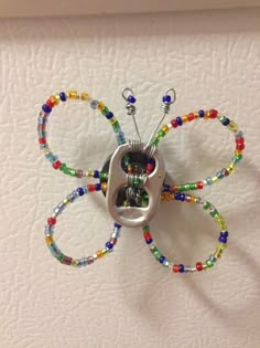 a metal butterfly with multicolored beads hanging from it's back end on a white wall