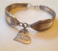 a silver bracelet with two charms and a heart on the clasp that says, peace