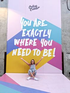 a woman sitting on the ground in front of a large sign that says you are exactly where you need to be