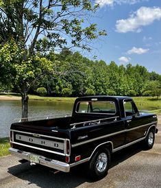 an old black truck parked next to a lake