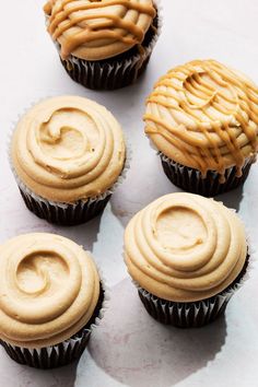 four cupcakes with peanut butter frosting in them on a white table top