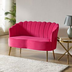 a pink couch sitting on top of a wooden floor next to a table with a lamp