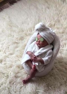 a baby wearing sunglasses and a towel wrapped around its head is laying on a white rug