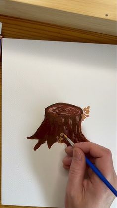 a person is painting a piece of art with brown paint on white paper and blue pencils