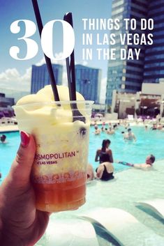 a person holding up a drink in front of a swimming pool with people on it