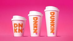 three coffee cups sitting next to each other on a pink background with the words dunkin