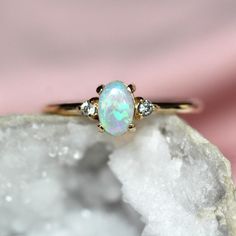 an opal and diamond ring sits on top of a rock