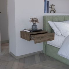 a nightstand with a book and vase on it next to a bed in a bedroom