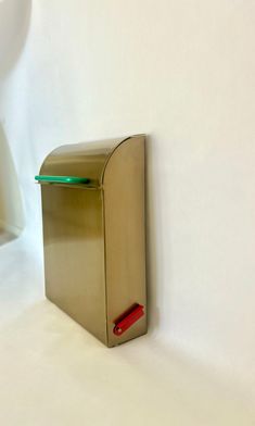 a metallic mailbox with a green light on the front and side, against a white wall