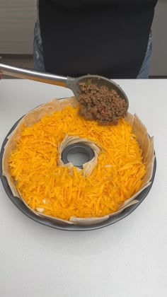 a person holding a spatula over a plate with cheese on it and ground beef in the middle