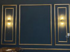 a room with blue walls and gold framed mirrors on the wall next to a table