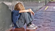 a young man sitting against a wall with his head on his hands and legs crossed