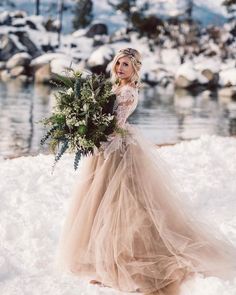 a woman in a wedding dress holding a bouquet standing in the snow with mountains in the background